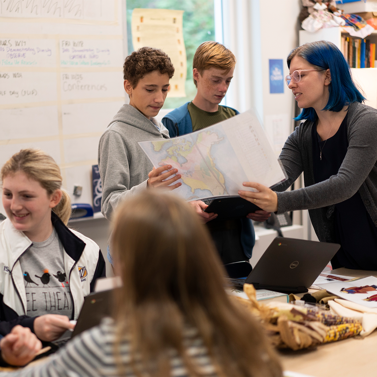 Two students holding map talk to the teacher