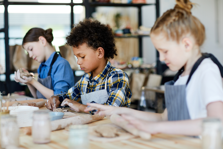 three students in art class using clay