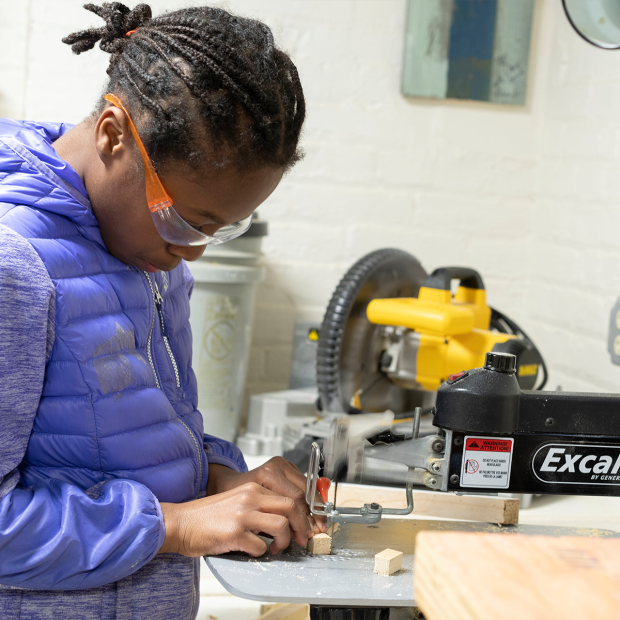 Student wearing safety goggles using an electric saw