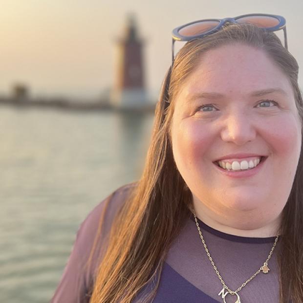 Julia Tuvin '09 standing outside at sunset with a lighthouse in the background
