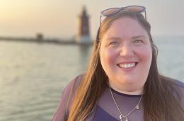 Julia Tuvin '09 standing outside at sunset with a lighthouse in the background