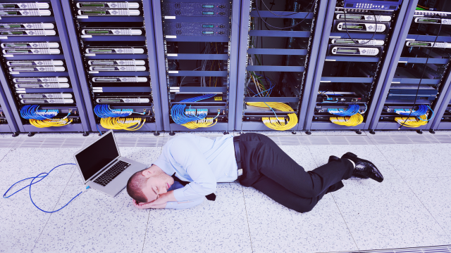 IT specialist asleep on floor in front of row of computer servers.