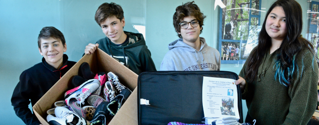 Four students hold suitcases full of donated clothes