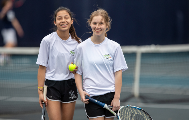 Two girls smiling on tennis court