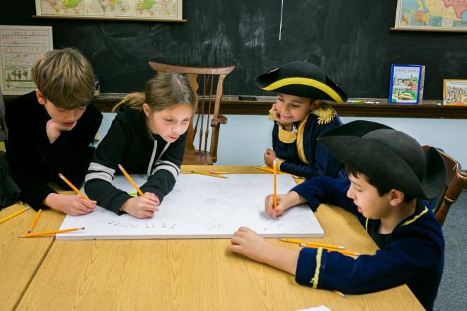 Students dressed in American Revolution gear work on project at table