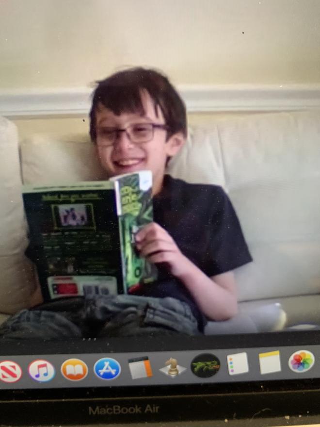 young boy student sitting on couch reading a book